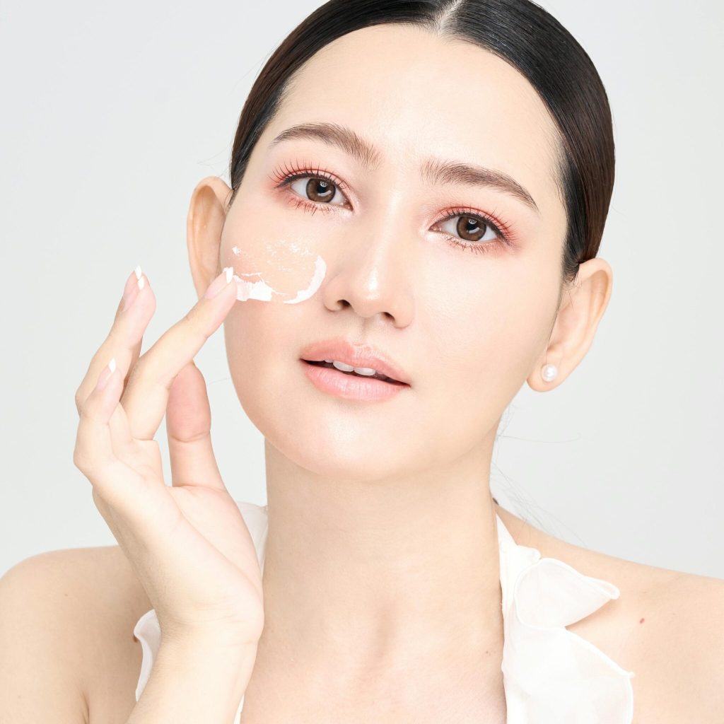 A young woman applies skincare cream to her face, promoting a healthy and radiant complexion.