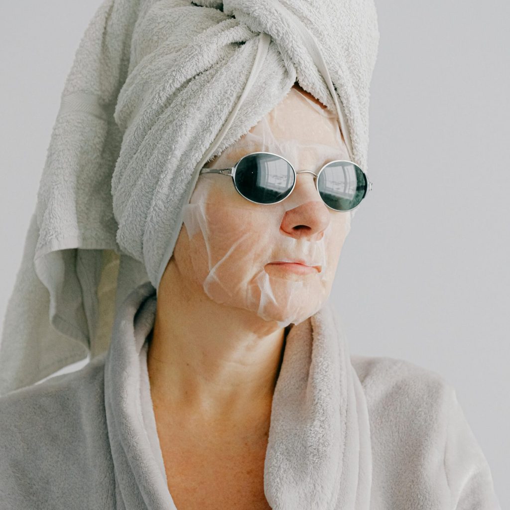 Senior woman in bathrobe with face mask and sunglasses enjoying a relaxing moment at home.