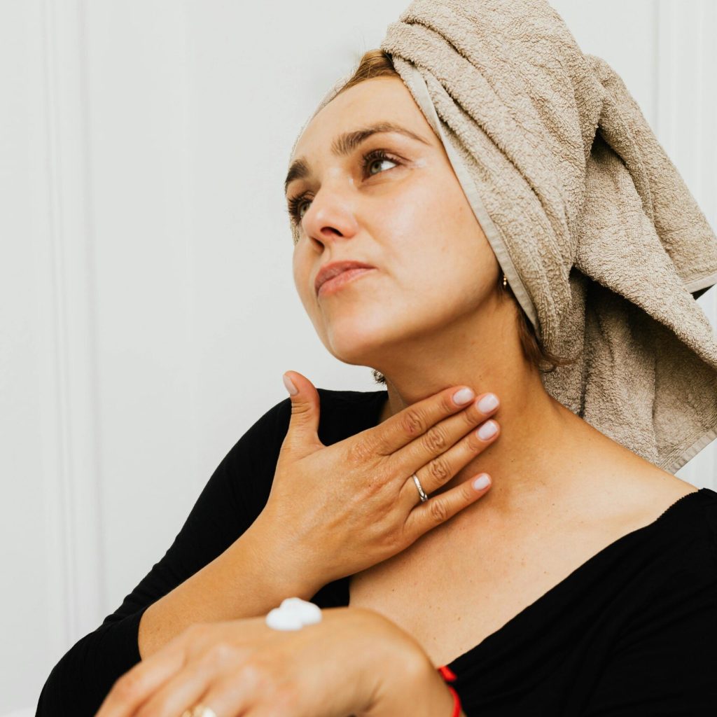 Woman with a towel on her head applying lotion to her neck post-bath.